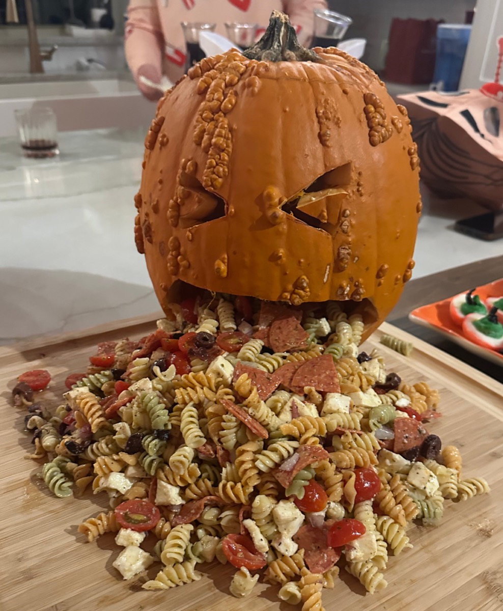 Tangy Italian pasta salad served in a barfing Halloween pumpkin carving on a wooden board