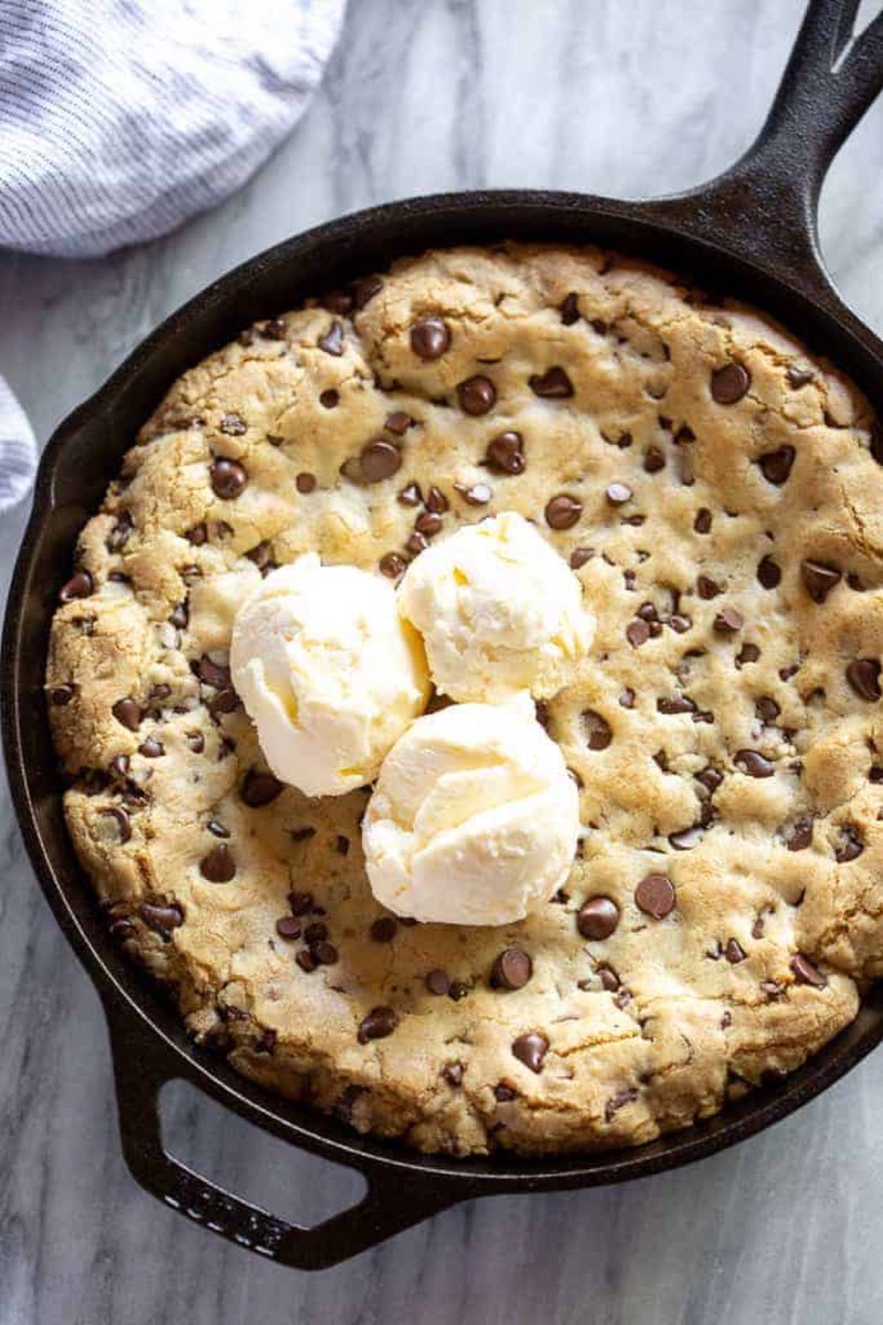 Warm chocolate chip skillet cookie in a cast iron pan topped with vanilla ice cream